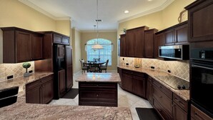 A kitchen with dark wooden cabinets, granite countertops, a central island, and built-in appliances including a microwave and oven.
