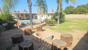 Patio trasero con piscina, palmeras y zona de fogata.