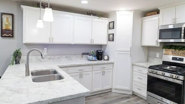 Una cocina moderna con armarios blancos, un lavamanos de acero inoxidable, horno empotrado y microondas.