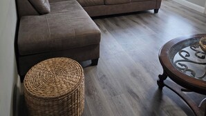 Una sala de estar con un sofá modular, un reposapiés redondo de mimbre, una mesa de centro con cubierta de vidrio y un espejo decorativo en la pared.