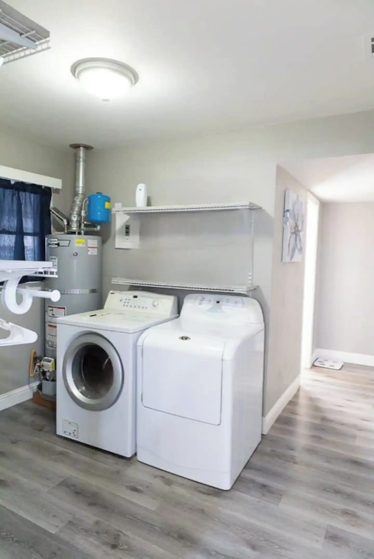 Une buanderie équipée de deux machines à laver blanches, d’un chauffe-eau et d’un système de ventilation.
