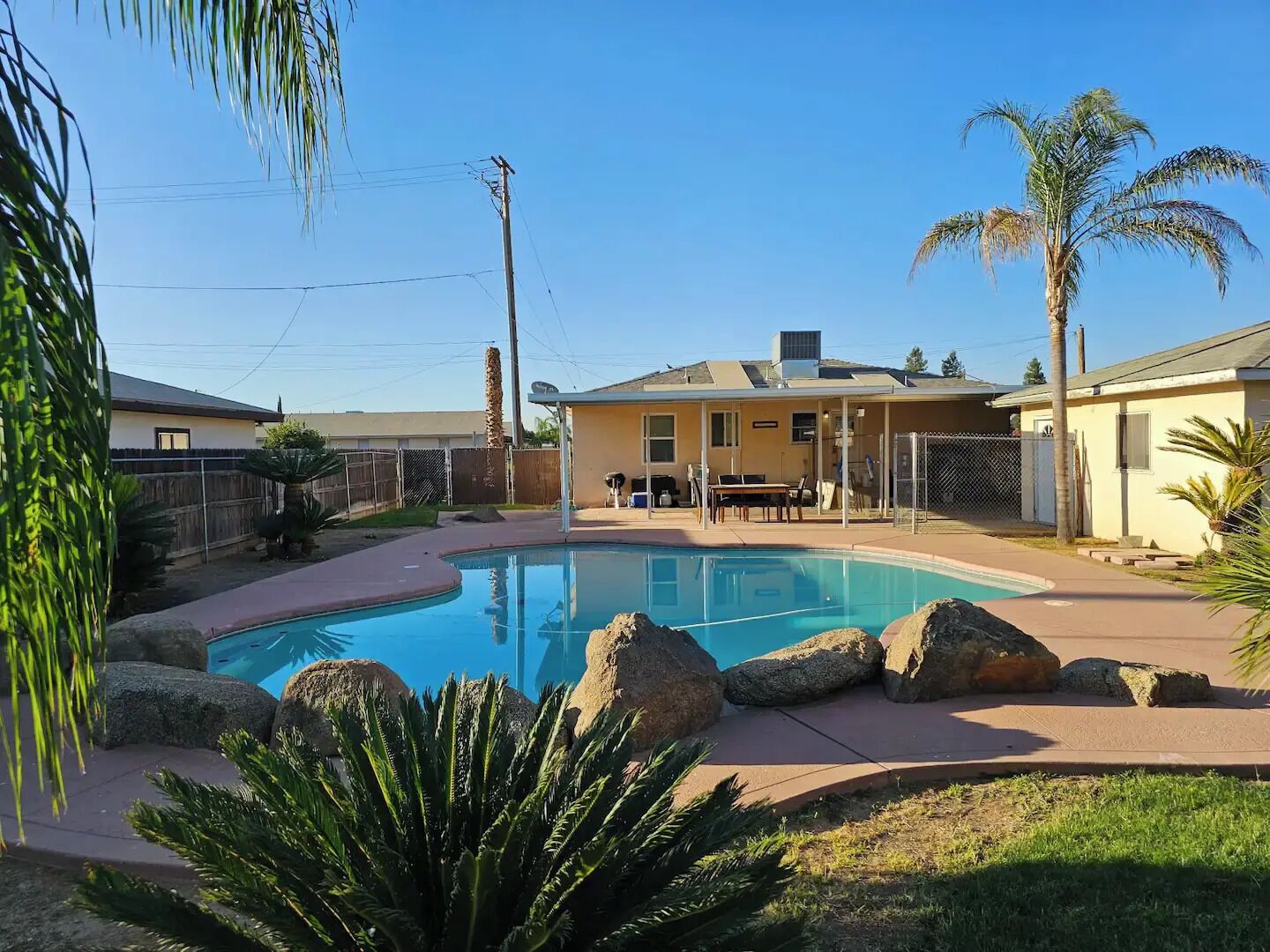 A backyard with a swimming pool, surrounded by rocks and palm trees.