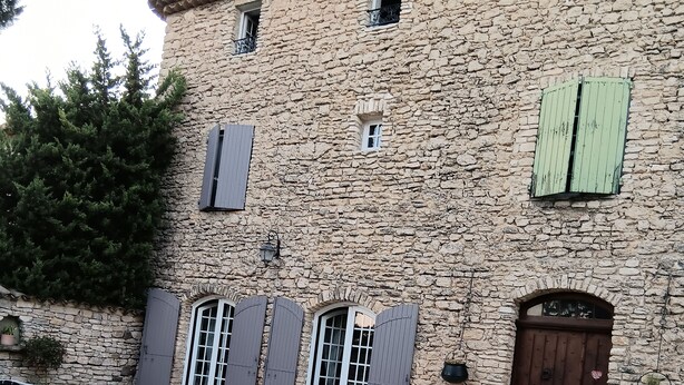Un bâtiment en pierre avec une cour recouverte de gravier, une porte en bois et une table en métal.