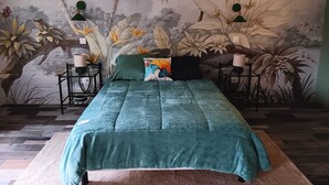 Une chambre à coucher avec un lit, une literie verte, une fresque murale à motifs floraux, deux tables de chevet avec des lampes et un plancher en bois.