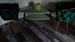 Une pièce dotée d’un parquet en bois foncé, d’une table ronde verte avec un coussin vert, et de deux fauteuils verts foncé à l’assise rembourrée et aux pieds en bois.