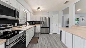 Una cocina moderna con electrodomésticos de acero inoxidable, armarios blancos y piso de madera claro.