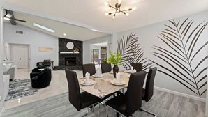 Un comedor con una mesa de mármol, sillas negras, un centro de mesa con planta y una lámpara moderna.