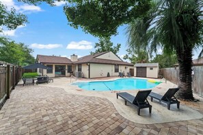 Un jardin avec une piscine, des chaises longues, un espace barbecue et une clôture en bois.