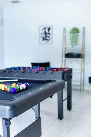 Une table de billard avec des billes, une échelle et un tableau encadré accroché au mur.