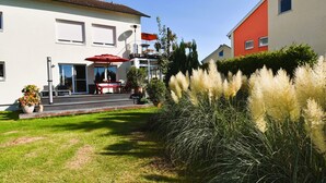A two-story building with a patio area featuring a red umbrella and outdoor seating. - Sunny 4-room garden apartment with pool near the lake for up to 6 people (Eriskirch)