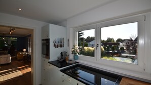 A modern kitchen with a large window, a built-in stove, and a dining area visible in the background. - Sunny 4-room garden apartment with pool near the lake for up to 6 people (Eriskirch)