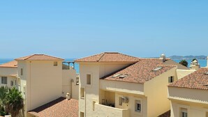 Un quartier résidentiel en bord de mer, avec des bâtiments aux toits de tuiles en terre cuite, un ciel d’un bleu limpide et une vue sur la mer.
