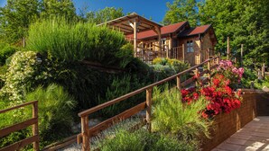 Une cabane en bois avec un toit rouge, entourée d’une végétation luxuriante et dotée d’un escalier en bois menant à une terrasse.