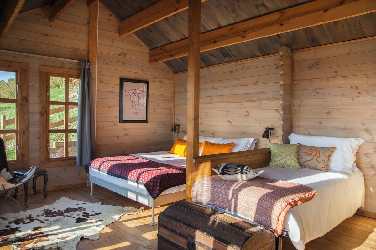 A cabin with two beds, a wooden ceiling, a framed picture on the wall, and a cowhide rug.