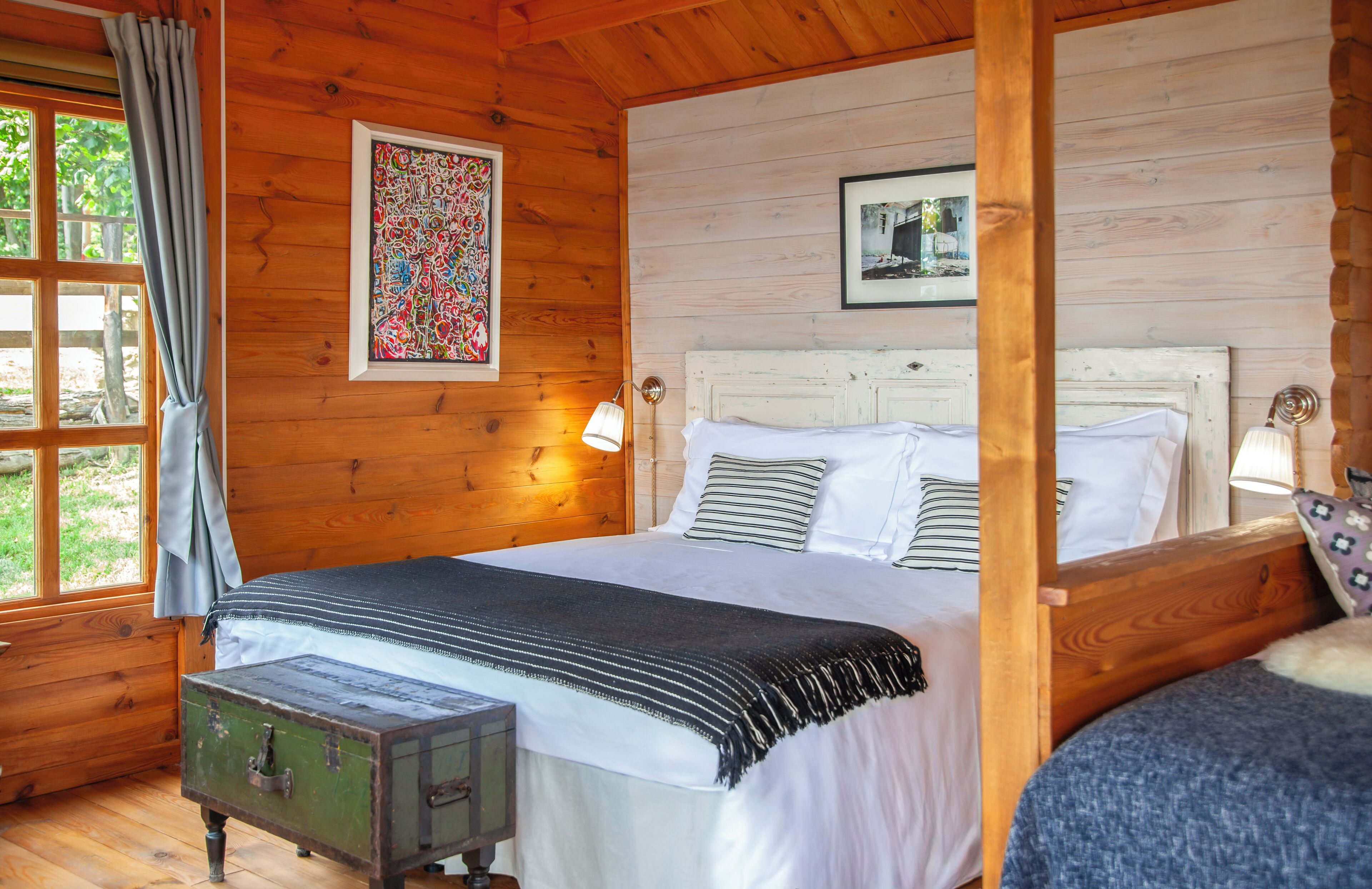 Ein Schlafzimmer einer Holzhütte mit einem großen Bett, einem kleinen Tisch und einem Fenster mit Vorhängen.
