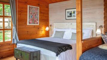 Ein Schlafzimmer einer Holzhütte mit einem großen Bett, einem kleinen Tisch und einem Fenster mit Vorhängen.