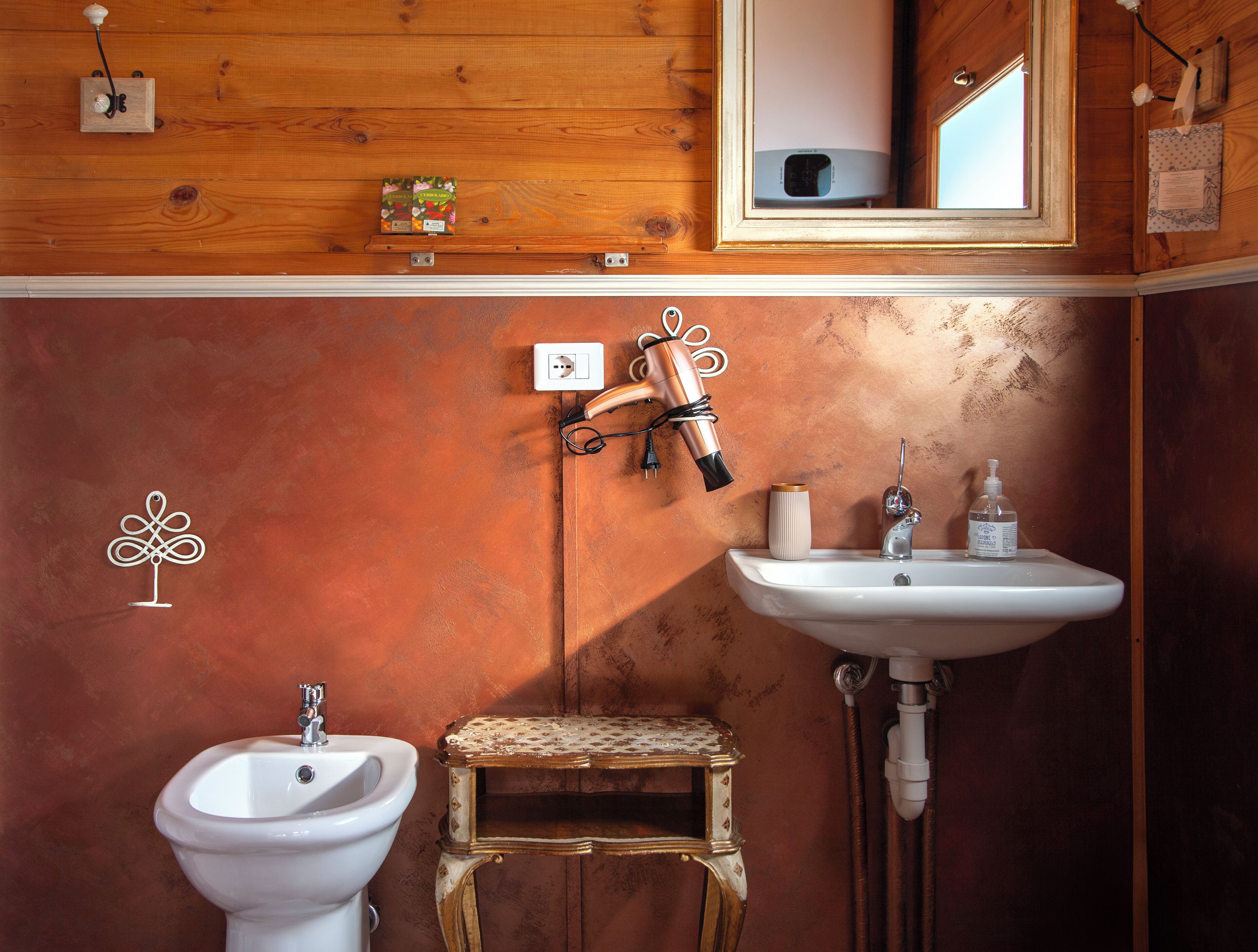 A bathroom with a wooden vanity, a white sink, a bidet, and a small stool.