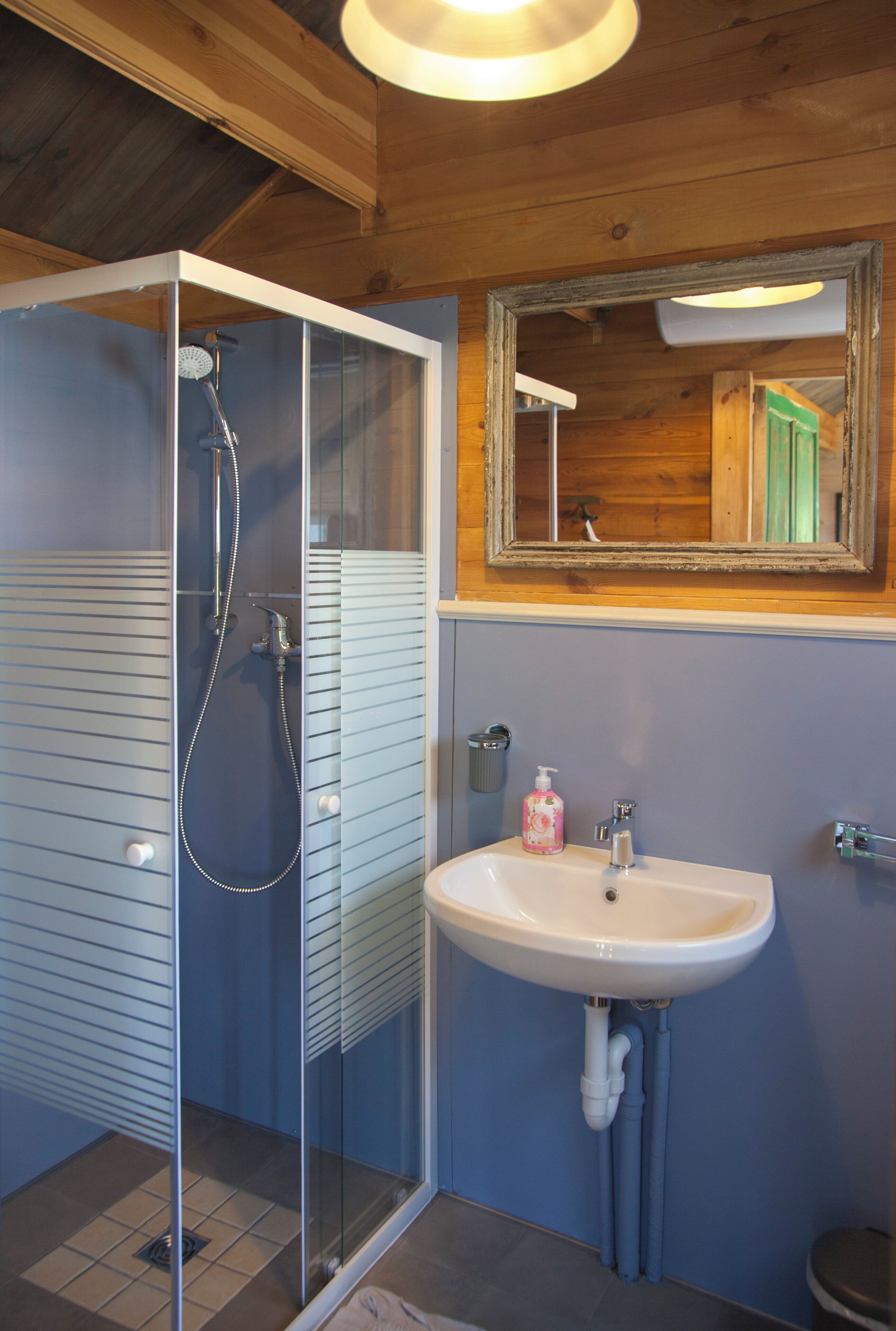 A bathroom with a glass shower enclosure, a sink with a mirror above it, and wooden ceiling beams.