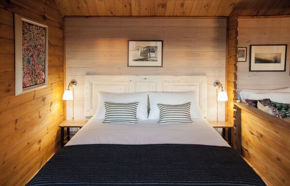 A wooden cabin-style room with a large bed, two bedside lamps, and framed pictures on the walls. - Pian del Mund (Borgomale)