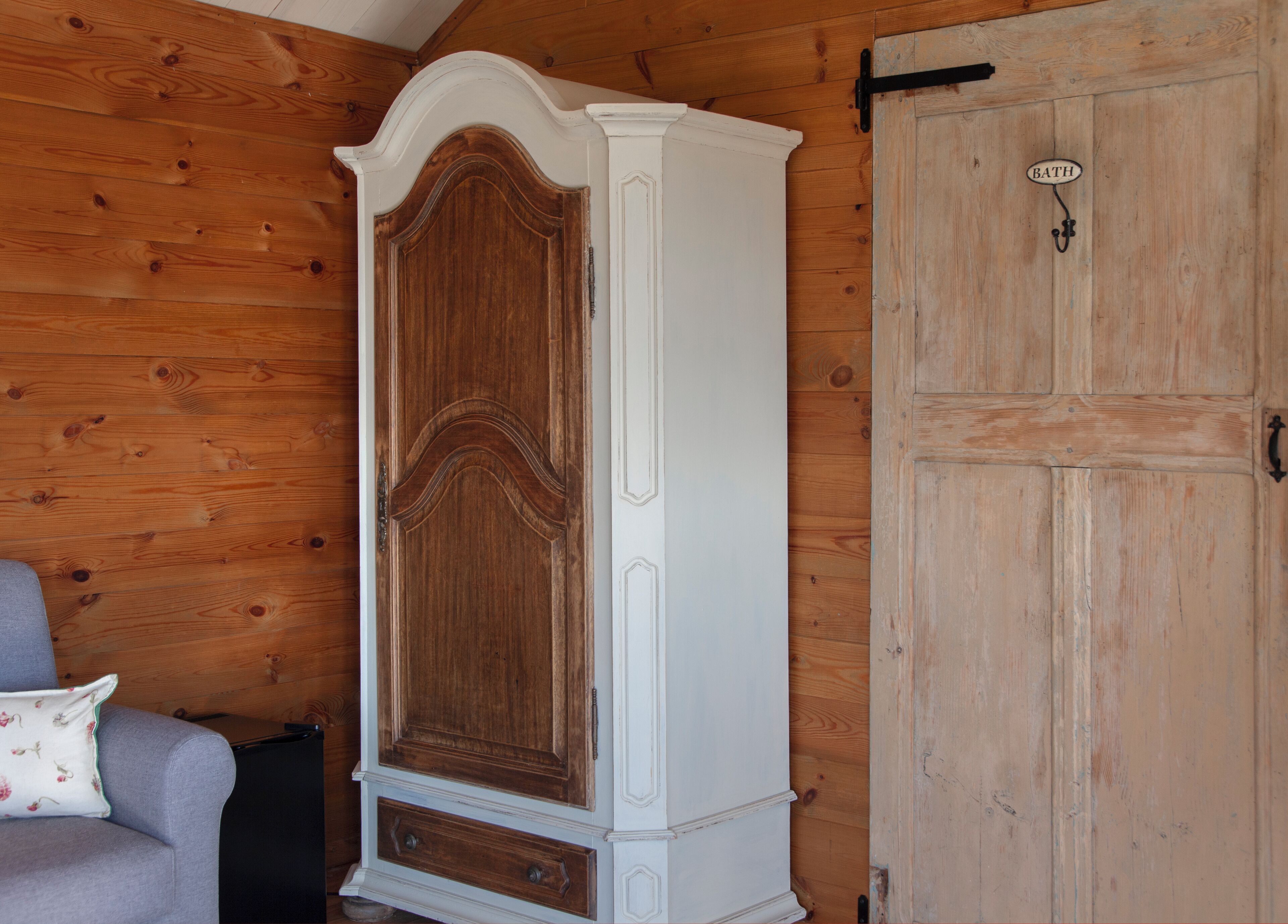 A wooden wardrobe with a white door and a wooden door with a 'BATH' sign.