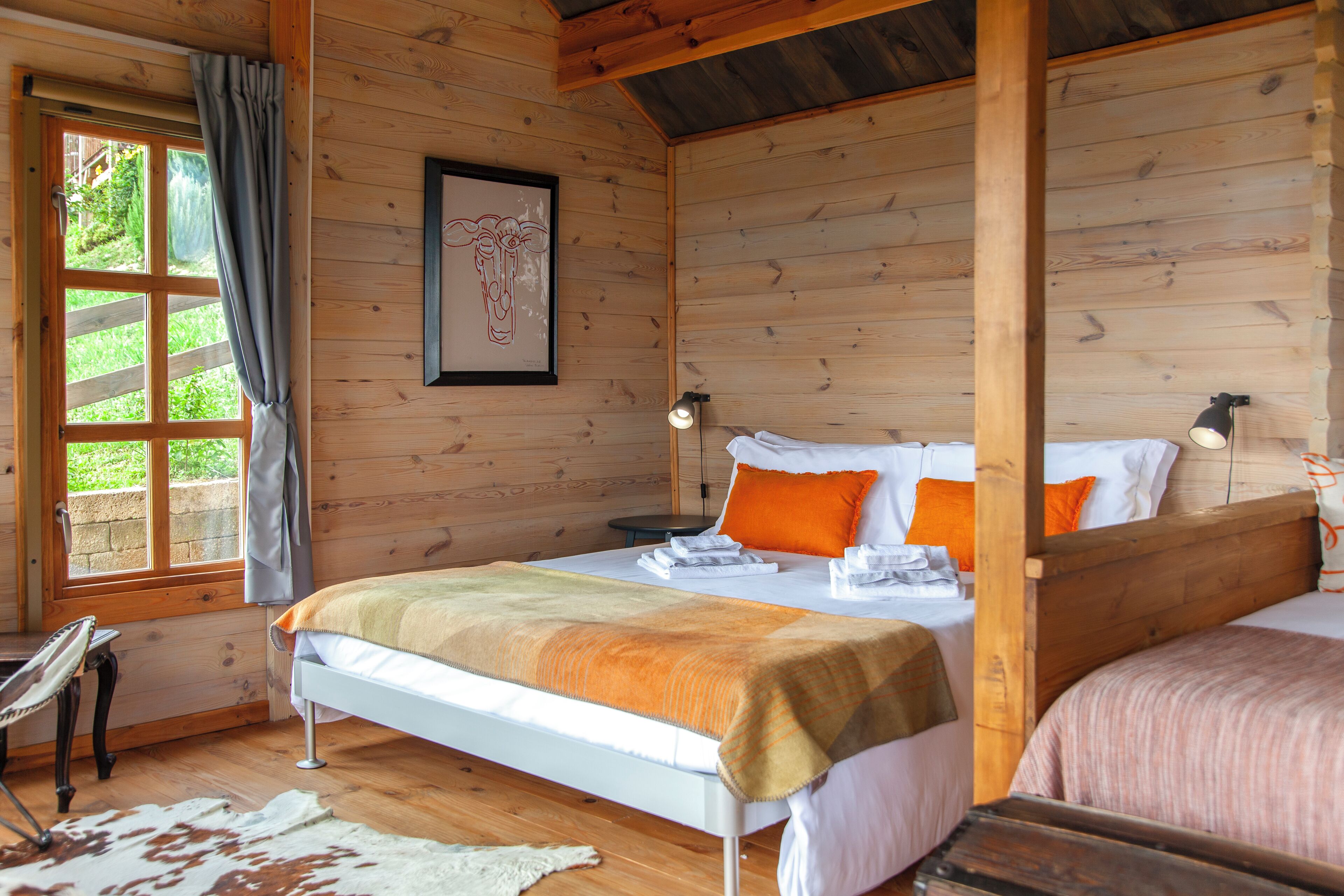 Un dormitorio de cabaña de madera con cama, escritorio y ventana con cortinas.