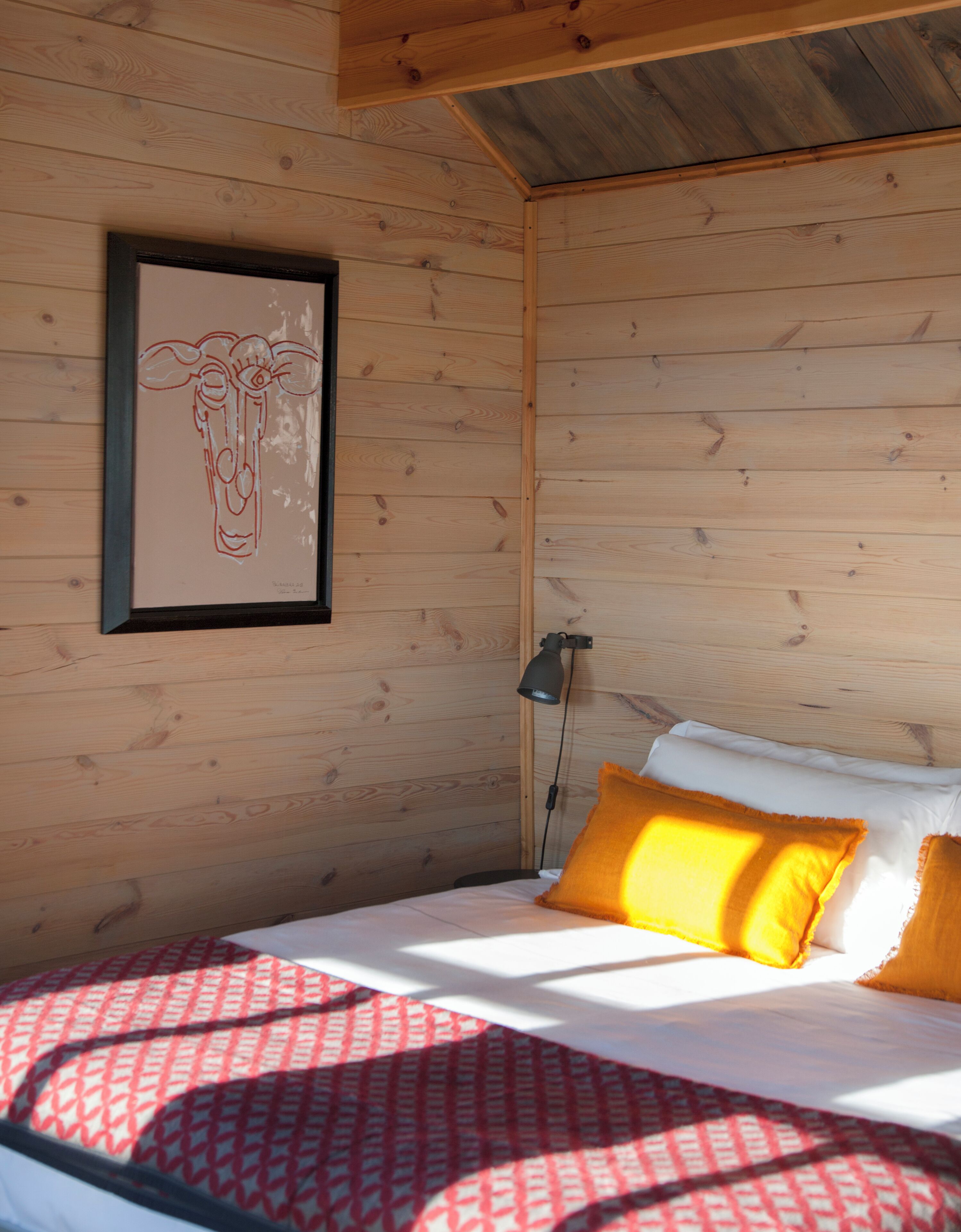 A wooden cabin room with a bed, a framed artwork, and a lamp.