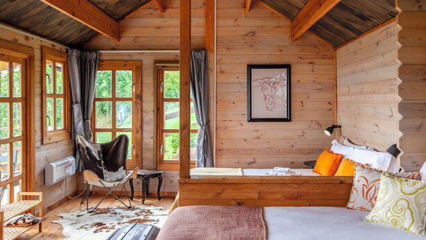 Une chambre dans une cabane en bois, avec un lit, une chaise, un bureau et une fenêtre avec des rideaux.