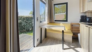 A modern kitchen with a built-in bench and a window overlooking a garden. - Wooden Tiny House with terrace, pool, wifi, pets, parking - 200m from the beach (Jullouville)