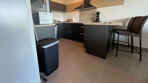 A compact kitchen with a built-in stove, a coffee maker, and a trash bin.