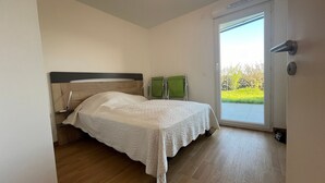 A bedroom with a bed, a green chair, and a sliding glass door leading to a balcony.