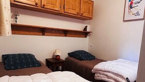 Ein Zimmer mit zwei Betten, Holzschränken darüber, einem kleinen Tisch mit einer Lampe und einem gerahmten Bild an der Wand.