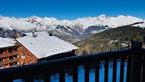 Ein Bergresort mit schneebedeckten Gipfeln, einer Holzterrasse und einem Gebäude mit roter Fassade.