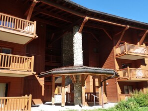 A wooden lodge with multiple balconies, a central stone pillar, and a covered outdoor area.