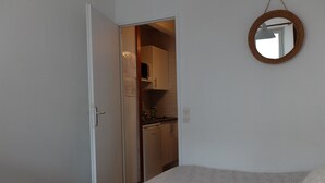 Ett sovrum med en säng, en garderob och ett köksutrymme som syns genom en öppen dörr.