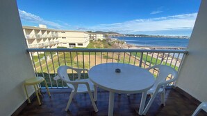 Een balkon met een ronde tafel en twee stoelen, met uitzicht op een strand en gebouwen.