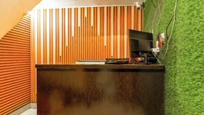 A reception desk with a wooden slat wall behind it, a computer monitor, and a keyboard on the desk. - Hotel Kashi Grand Inn (Varanasi)