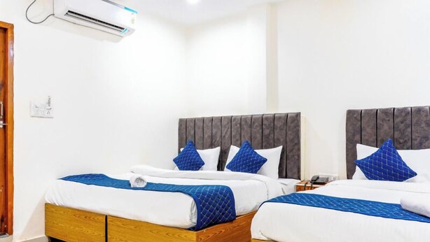 A hotel room with two beds, each with a wooden frame and white bedding. There is a wall-mounted air conditioner above the beds. - Hotel Kashi Grand Inn (Varanasi)
