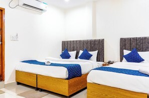 Une chambre d’hôtel avec deux lits, chacun doté d’un cadre en bois et de draps blancs. Un climatiseur mural est fixé au-dessus des lits.