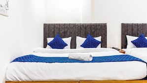 A double bed with a wooden headboard, white bedding, and blue patterned pillows. - Hotel Kashi Grand Inn (Varanasi)