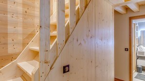 A wooden staircase with a handrail, leading to a room with a wooden floor and a door with a handle.
