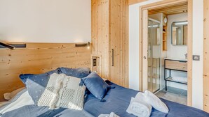 A bedroom with a wooden headboard, a bed with blue bedding, and a bathroom visible through an open door.