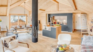 A spacious living area with a high ceiling, a central black column, a kitchen area with modern appliances, and a cozy seating arrangement.