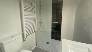 Een moderne badkamer met een douchecabine van glas, een wit toilet en een witte wastafel.