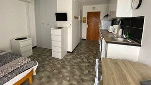 Een kleine hotelkamer met een bed, bureau, kitchenette en televisie.