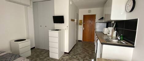 Una habitación de hotel compacta con cama, escritorio, kitchenette y televisor.