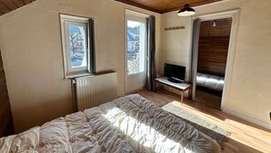 A bedroom with a bed, a TV on a small table, and a window with a view of buildings. - Bright duplex in the heart of Villard, 5 pax (Villard-de-Lans)