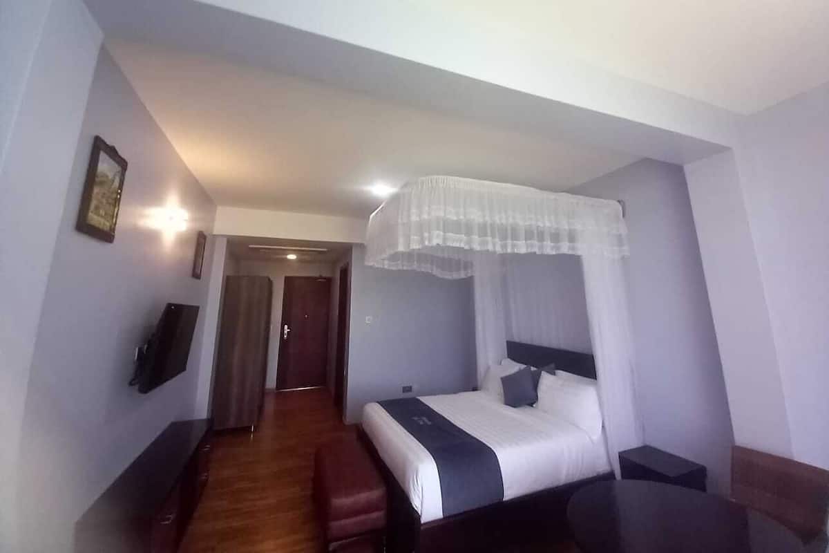 Ein Hotelzimmer mit Bett, Nachttisch und einem an der Wand befestigten Fernseher.