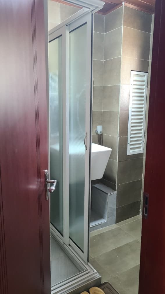 A bathroom with a glass shower enclosure, a white sink, and a tiled wall.