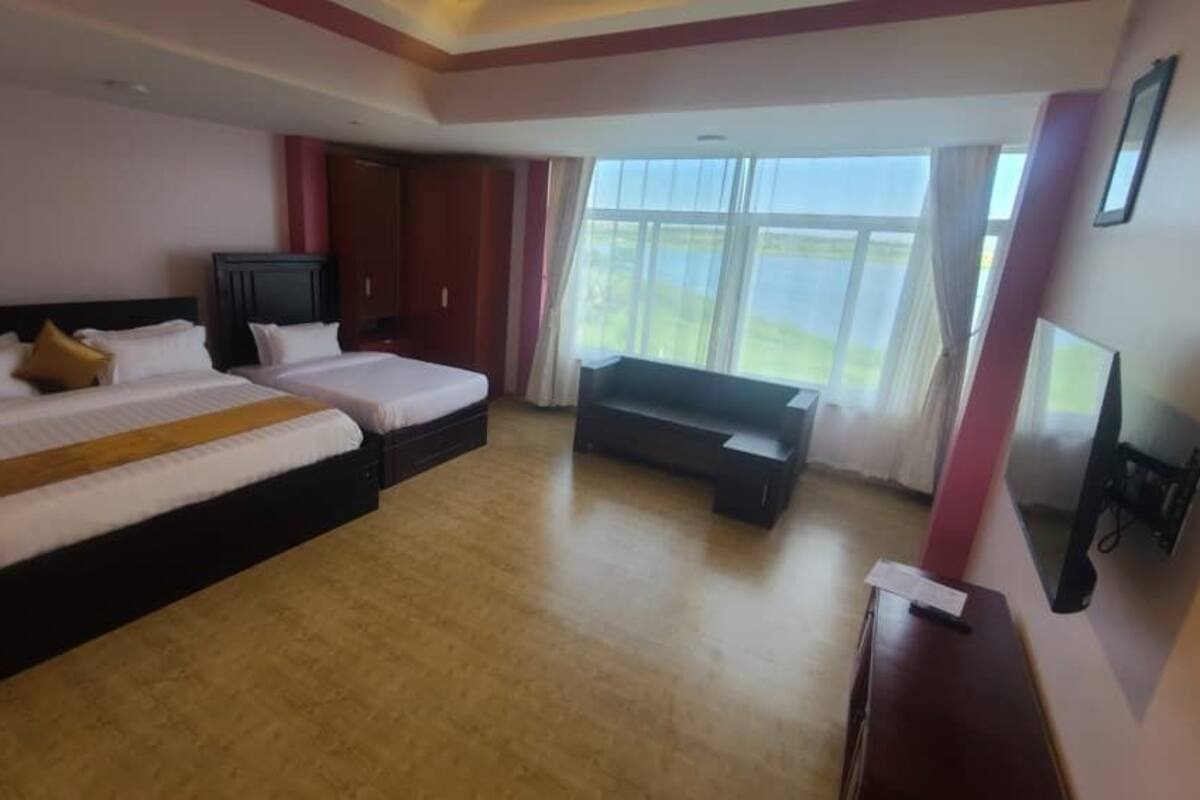 Ein Hotelzimmer mit zwei Betten, einer Couch, einem Fernseher und einem großen Fenster.