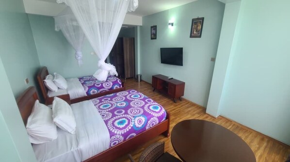 A room with two beds, a TV, a small table, and a chair. - Majestic Nile Hotel (Pakwach)